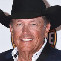 Ein älterer Mann in einem schwarzen Cowboyhut und Anzug lächelt in die Kamera.