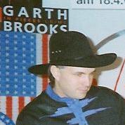 Garth Brooks in einem schwarzen Hut vor einem Werbeplakat mit seinem Namen.