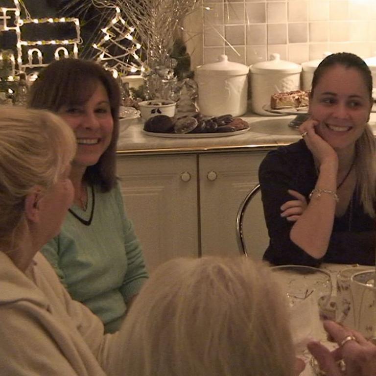 Eine Gruppe von Frauen lächelt während eines festlichen Treffens in einer gut dekorierten Küche mit einem Weihnachtsbaum im Hintergrund.