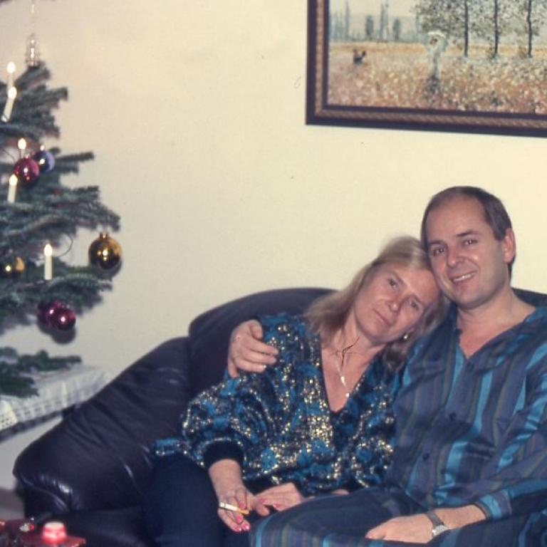 Drei Personen posieren auf einer Couch neben einem geschmückten Weihnachtsbaum und einem gerahmten Bild im Hintergrund.