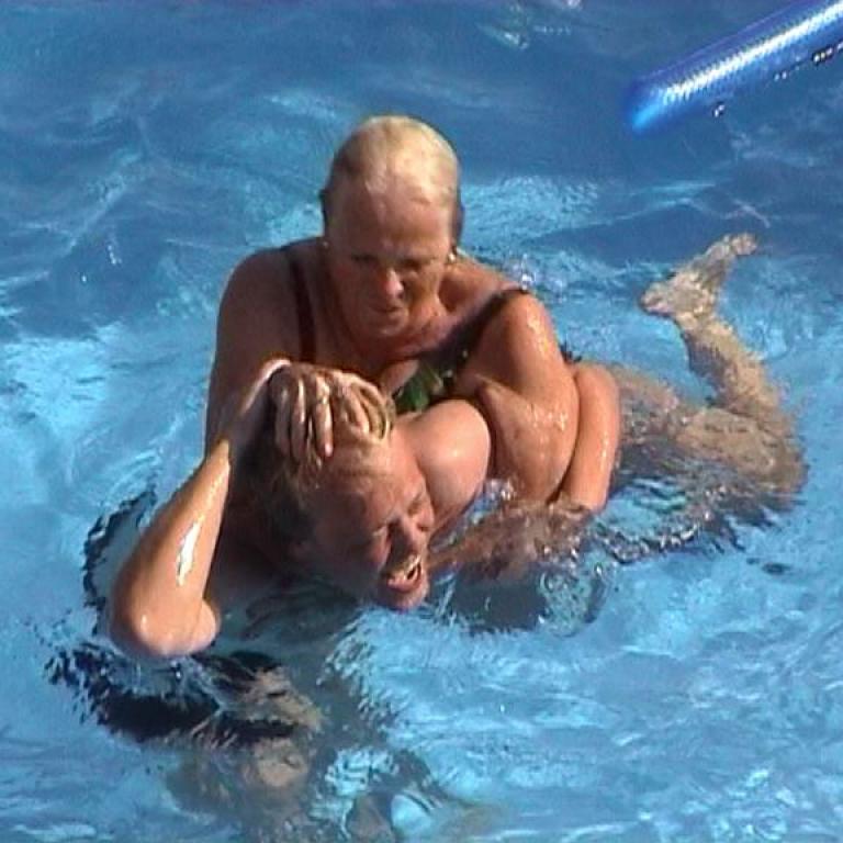 Zwei Personen in einem Schwimmbecken, bei dem eine Person die andere fest hält und unterstützt.