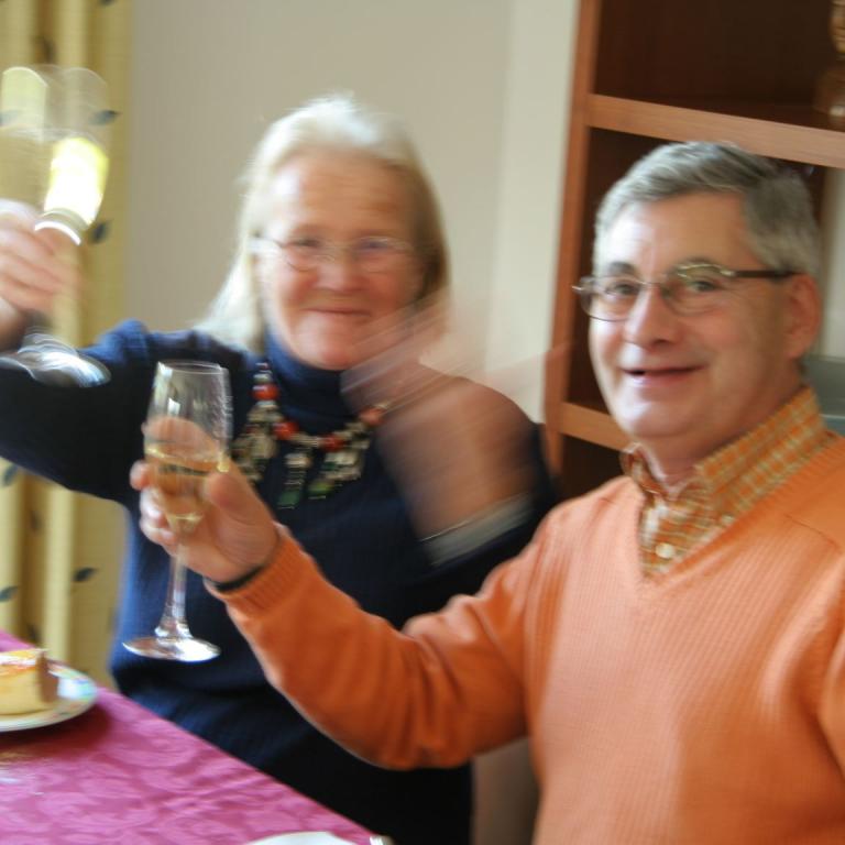 Eine Familie oder Gruppe von Freunden sitzt bei einer Feier und hält Gläser in der Hand.