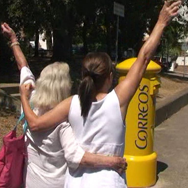 Drei Frauen treffen sich draußen in einem Park und umarmen sich herzlich neben einem gelben Schild.