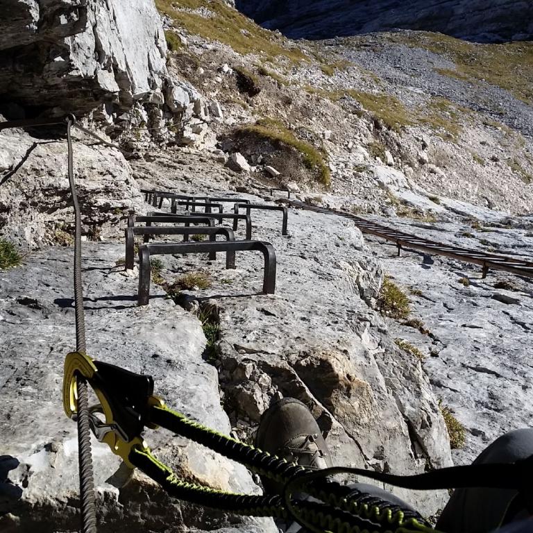Ein exponierter Wanderweg mit Seilen und Geländern an einem steilen Berghang.