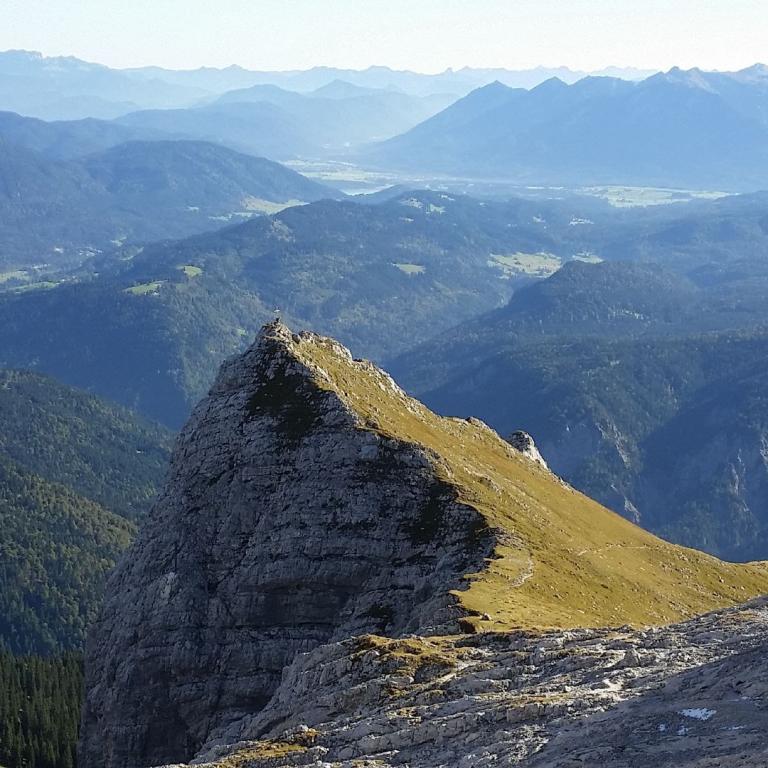 Panoramablick von einem markanten Berggrat auf eine weite, geschichtete Berglandschaft.