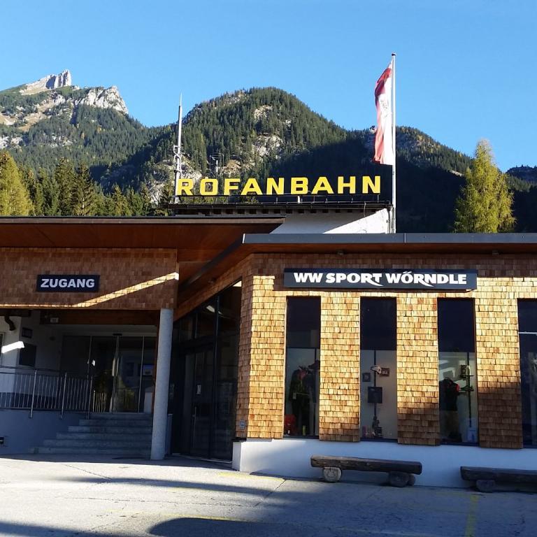 Der Eingangsbereich der Profanbahn mit Schildern für Kasse und Zugang vor einer bergigen Landschaft.