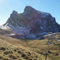 Eine imposante, schneebedeckte Bergkette überragt sanfte, grasbewachsene Hänge unter einem klaren blauen Himmel.