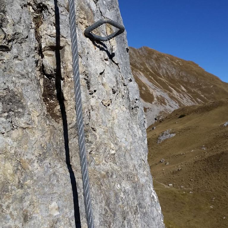 Seil und Karabiner an einer steilen Felswand mit Bergpanorama im Hintergrund