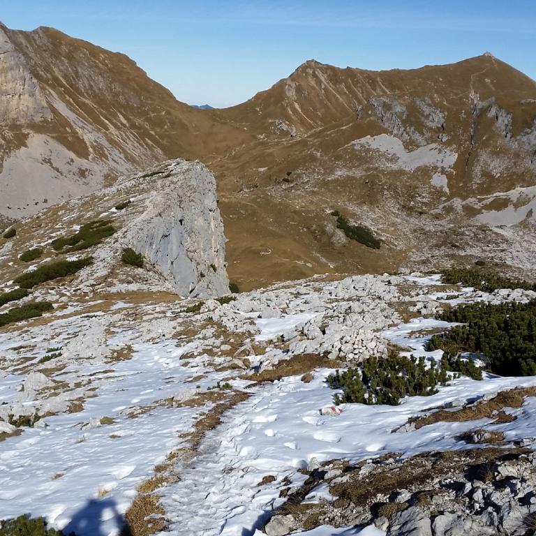 Hohe Berglandschaft mit schneebedecktem Vordergrund und markanten Felsformationen im Hintergrund.