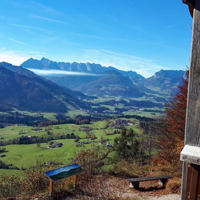 Panoramablick über eine grüne Hügellandschaft mit Bergkette und einem Wegweiser im Vordergrund.