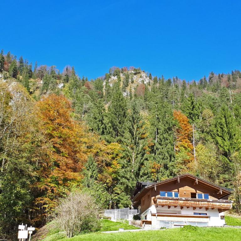 Ein modernes Haus vor einer Kulisse aus herbstlich gefärbtem Wald in den Bergen unter einem blauen Himmel.