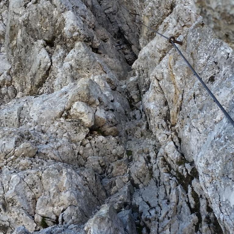 Nahaufnahme einer zerklüfteten, grauen Felswand, die einen vertikalen Abgrund bildet, mit einem darüber gespannten Seil.