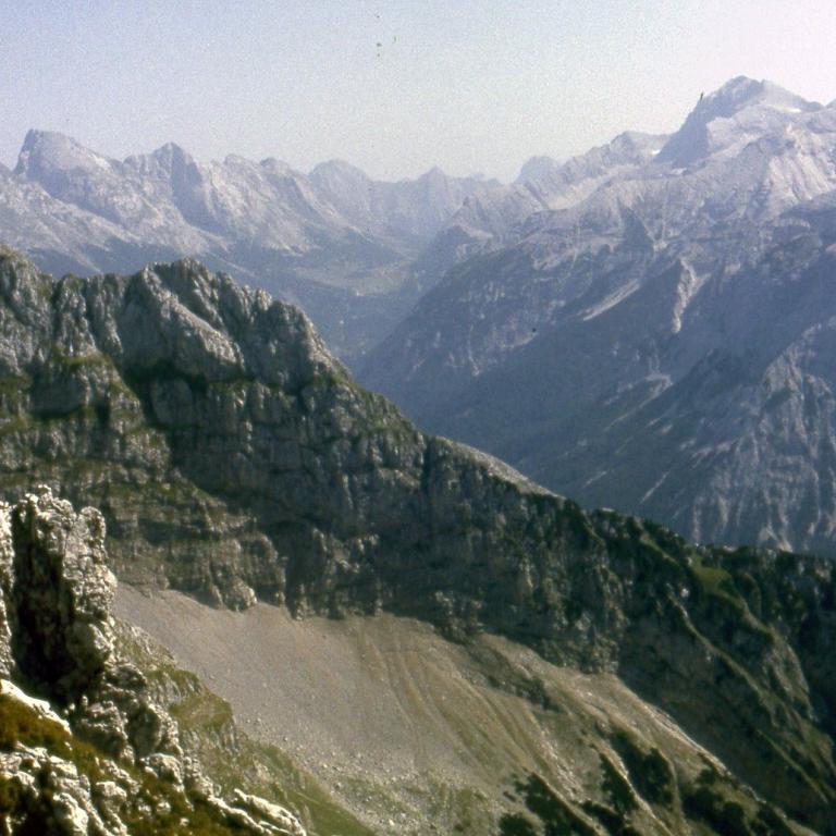 Weitläufiges Panorama einer Gebirgskette mit tiefen Tälern und steilen Hängen.