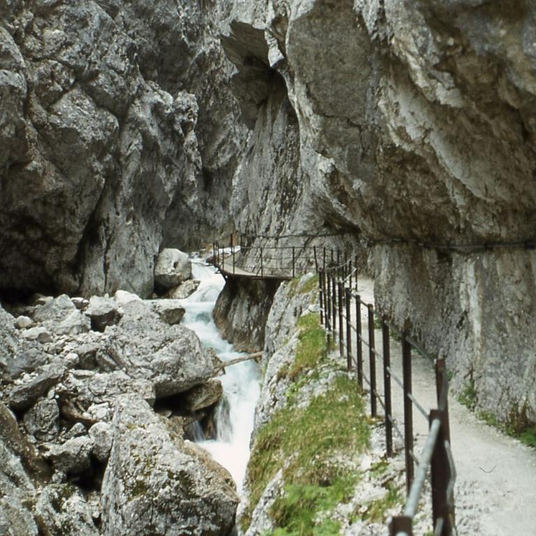 Schmale Steg zwischen steil abfallenden Felswänden mit einem rauschenden Wasserfall.