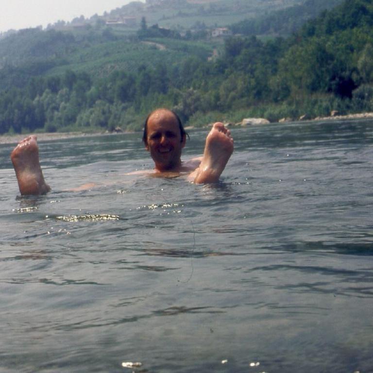 Ein Mann steht in einem Fluss, mit einer bewaldeten Hügellandschaft im Hintergrund.