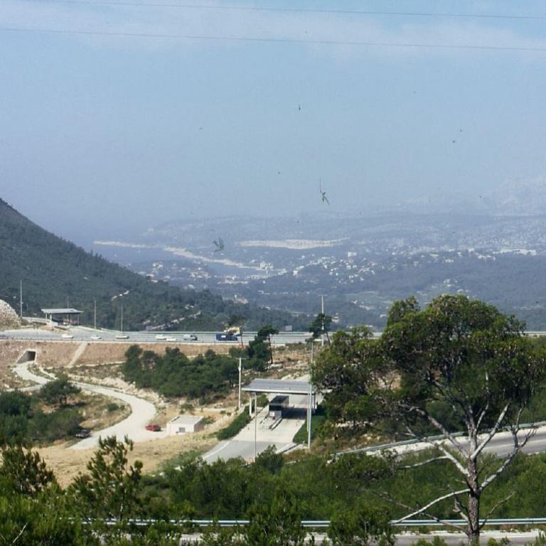 Panoramaaussicht auf ein Bergmassiv links und eine weitläufige, städtische Ebene im Hintergrund mit einer Straße im Vordergrund