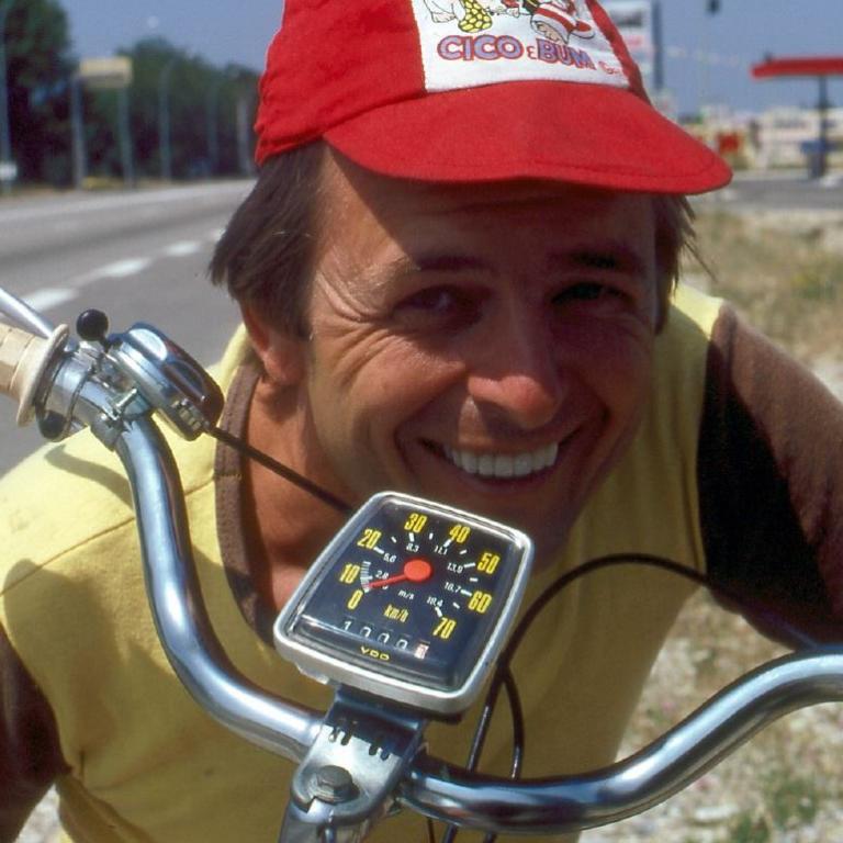 Ein lächelnder Mann sitzt auf einem Motorrad, das Armaturenbrett ist im Vordergrund sichtbar.