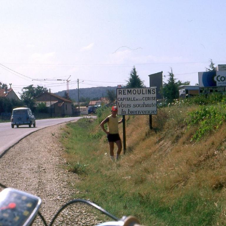 Ein Mann steht auf einem Weg neben einer Straße in einer ländlichen Vorstadtumgebung.