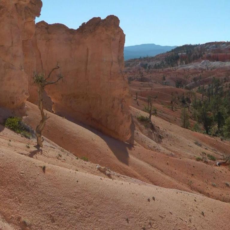 Dramatisches Panorama von ockergelben Klippen und roten Badlands-Hängen unter blauem Himmel.