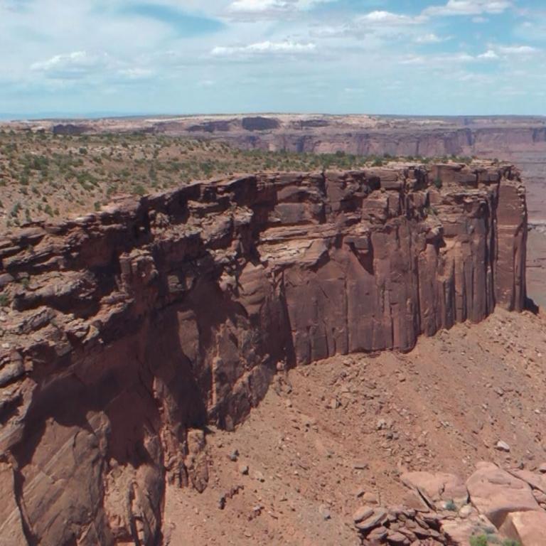 Eine weite Aufnahme des Canyonrandes mit steilen Felswänden und einer kargen Wüstenlandschaft.