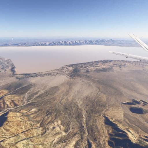 Aussicht von einem Flugzeug auf eine große, flache Salzpfanne mit trockener, hügeliger Landschaft im Vordergrund
